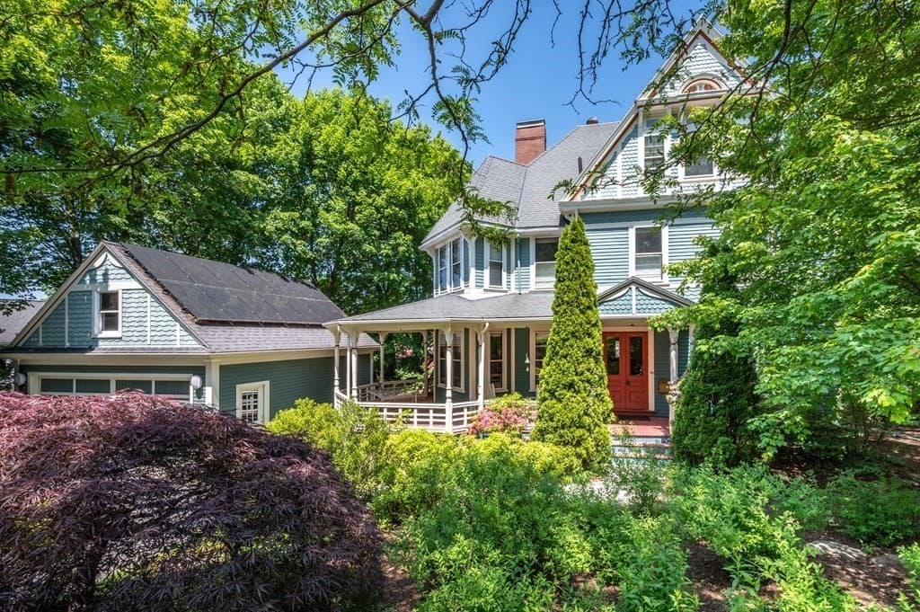 Teal Victorian home with a wraparound porch and red front door framed by lush green trees