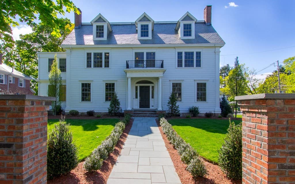 White Colonial Revival home with brick gate pillars and a bluestone walkway lined with clipped shrubs